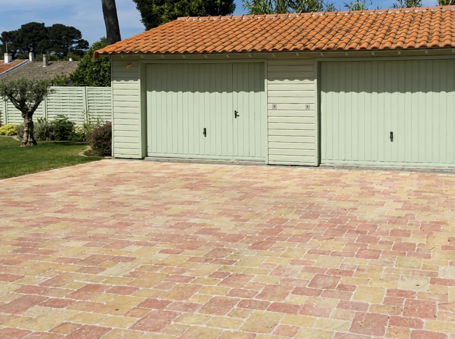 Allée de garage extérieure pavée de dalles en béton moulé aspect vieilli, tons ocre-rouge et jaune sable