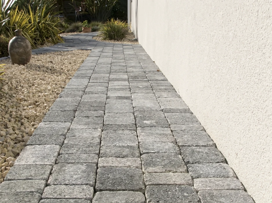 Allée extérieure pavée longeant un mur en crépi blanc