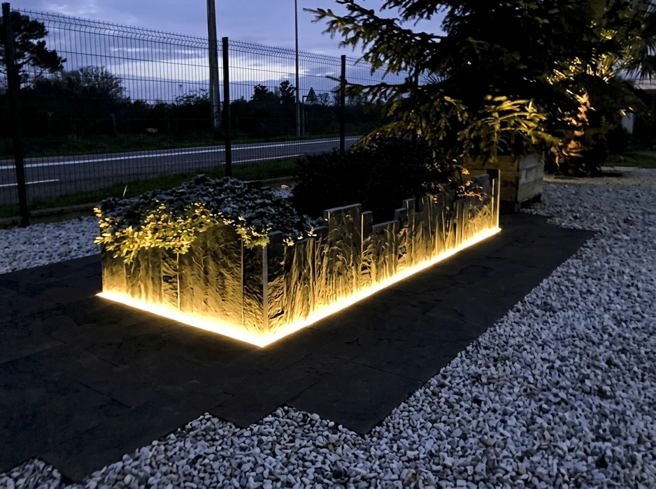 Jardinière rectangulaire surélevée en pierre naturelle texturée, illuminée au crépuscule par un bandeau LED warm white intégré à la base