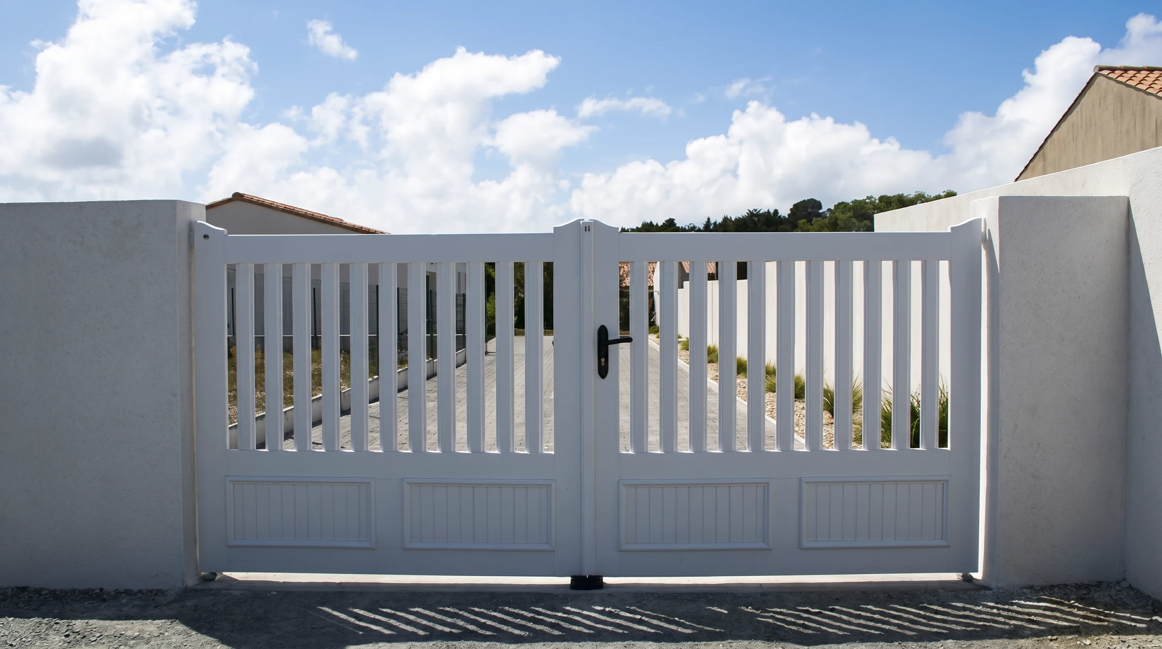 Portail double battant blanc en PVC ou aluminium laqué, monté entre deux piliers en béton enduit blanc